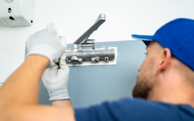 Cerrajero montando el brazo cierrapuertas en la puerta del portal de una comunidad de vecinos