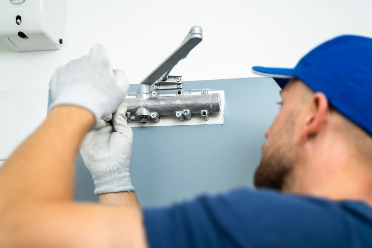 Cerrajero montando el brazo cierrapuertas en la puerta del portal de una comunidad de vecinos